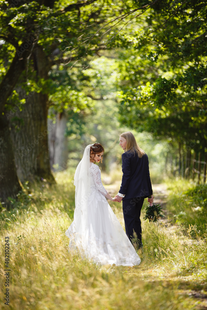 Wedding day of Young couple in a summer garden. Bride and Groom tender holding each other. Redhead woman and blonde man with long hairs. Wedding family outdoor walk. Love and tenderness