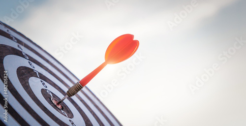 Close up shot red darts arrows in the target of dartboard center on dark blue sky background. Business target or goal success and winner concept.