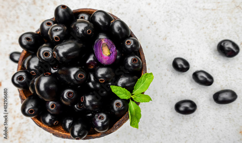 Black ripe Syzygium cumini fruits. Dark black java plum in a wood bowl at isolated white background. Green mint leaf on top of some large java plums.