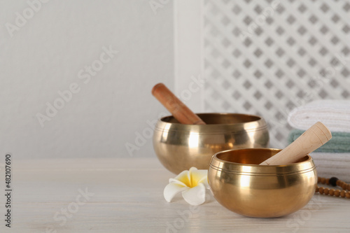 Golden singing bowls, mallets and flower on white wooden table, space for text