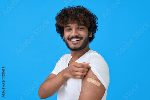 Happy young adult indian latin man showing bandage plaster on arm after getting vaccination isolated on blue Fototapete