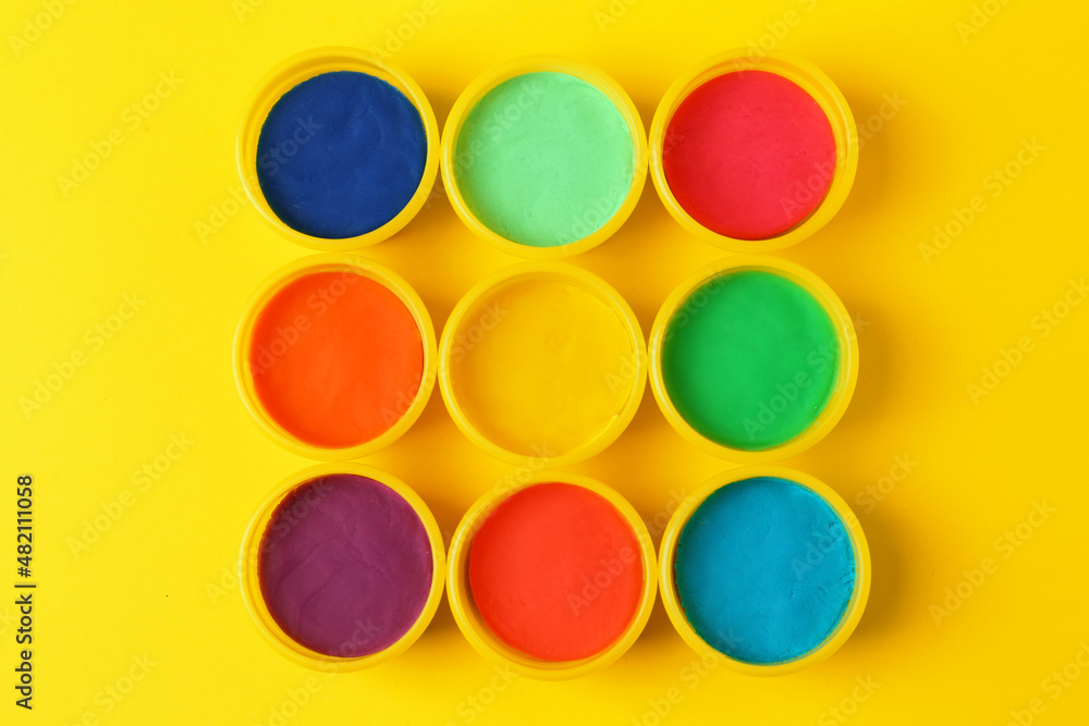 Plastic containers with colorful play dough on yellow background, flat lay Plastic containers with colorful play dough on yellow background, flat lay