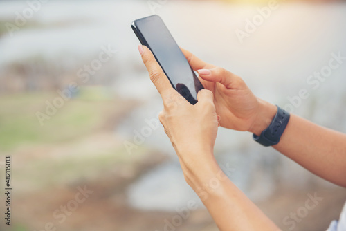 woman stand on the banks of the lake using her cell phone send message sms e-mail, taking pictures, Video call, Asian woman hiker in front smiling happy, Woman hiking in woods, warm summer day.