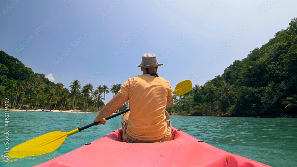 Man with sunglasses and hat rows pink plastic canoe along sea ag