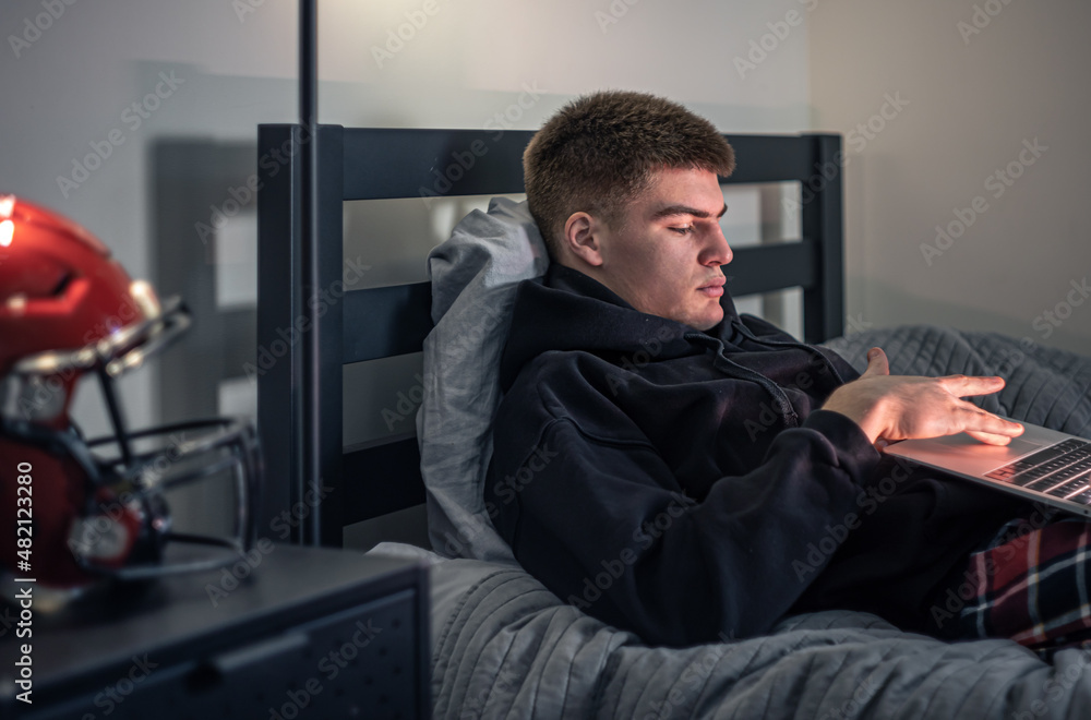 A teenager guy sits in a room on a bed and uses a laptop. A teenager guy sits in a room on a bed and uses a laptop.