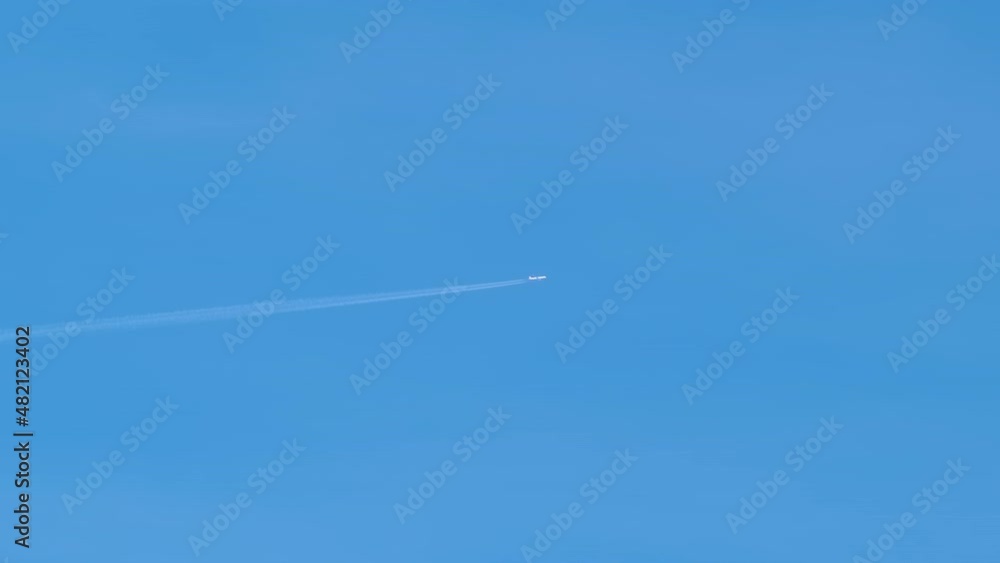Distant passenger jet plane flying on high altitude on clear blue sky leaving white smoke trace of contrail behind. Air transportation concept Distant passenger jet plane flying on high altitude on clear blue sky leaving white smoke trace of contrail behind. Air transportation concept