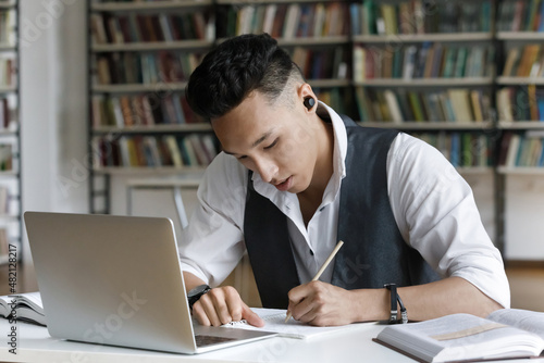 Canvastavla Focused serious Asian student guy with wireless earphones writing notes, researc