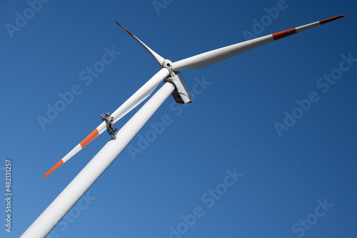 Red and white wind turbine for power generation with a maintenance team working in a basket on one blade with a blue sky in the background