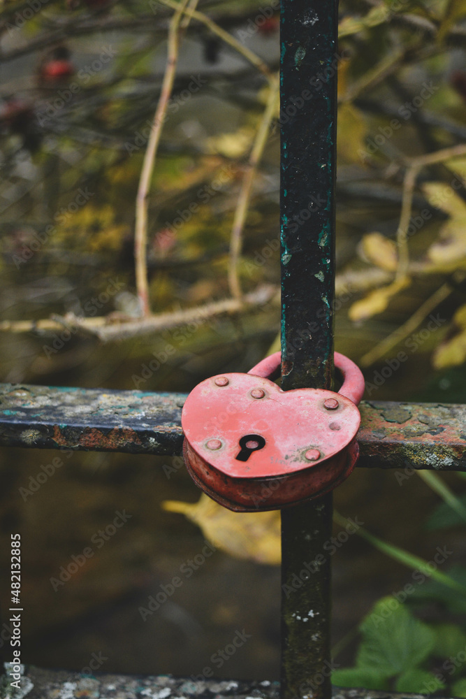 Obraz premium red heart shaped metal padlock on the bridge in autumn with yellow leaves on background