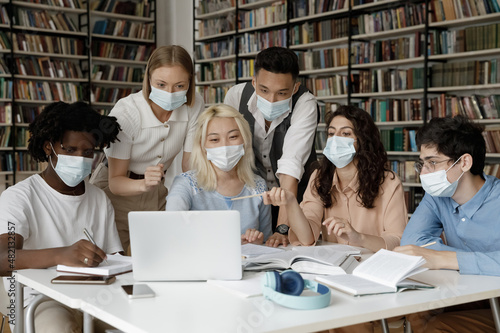Wallpaper Mural Interracial group of gen Z students wearing facial medical masks sitting at laptop in college library, watching online presentation, discussing learning webinar, working on project together Torontodigital.ca