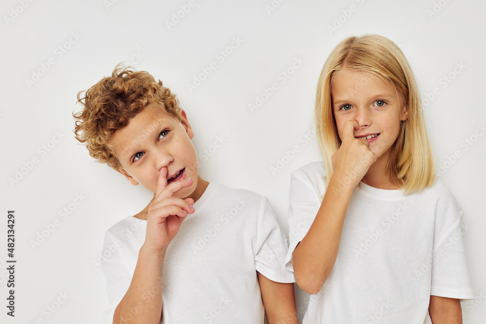 Photo of two children in white T-shirts are standing next to beige background Photo of two children in white T-shirts are standing next to beige background