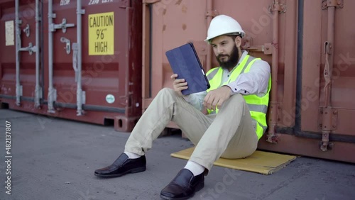 Wallpaper Mural Male engineers leaning on containers while working. He was upset after looking at some information from his tablet, and he took off his helmet in transportation logistic concept Torontodigital.ca