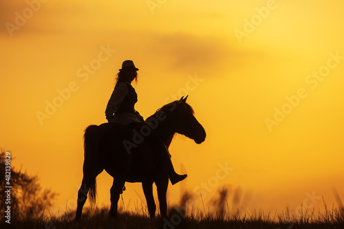 silhouette of a woman with hat riding a horse in the setting sun