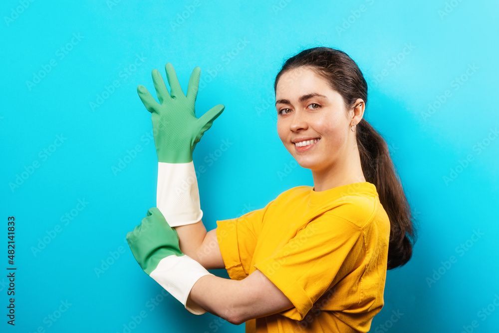 Portrait of a beautiful smiling Caucasian young woman wearing a rubber gloves. Blue background. Concept of cleaning service Portrait of a beautiful smiling Caucasian young woman wearing a rubber gloves. Blue background. Concept of cleaning service
