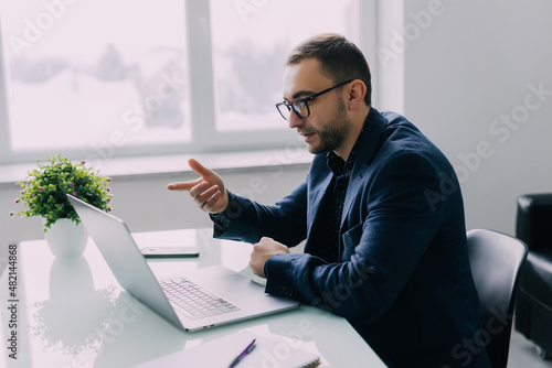 Fototapeta Focused young businessman in eyewear wearing headphones, holding video call with clients on laptop