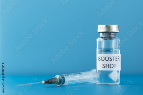 booster shot of coronavirus vaccine in a vial on blue background
