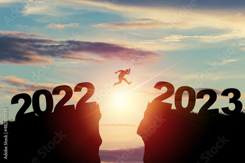 Welcome merry Christmas and happy new year in 2023,Silhouette Man jumping from 2022 cliff to 2023 cliff with cloud sky and sunlight. photo