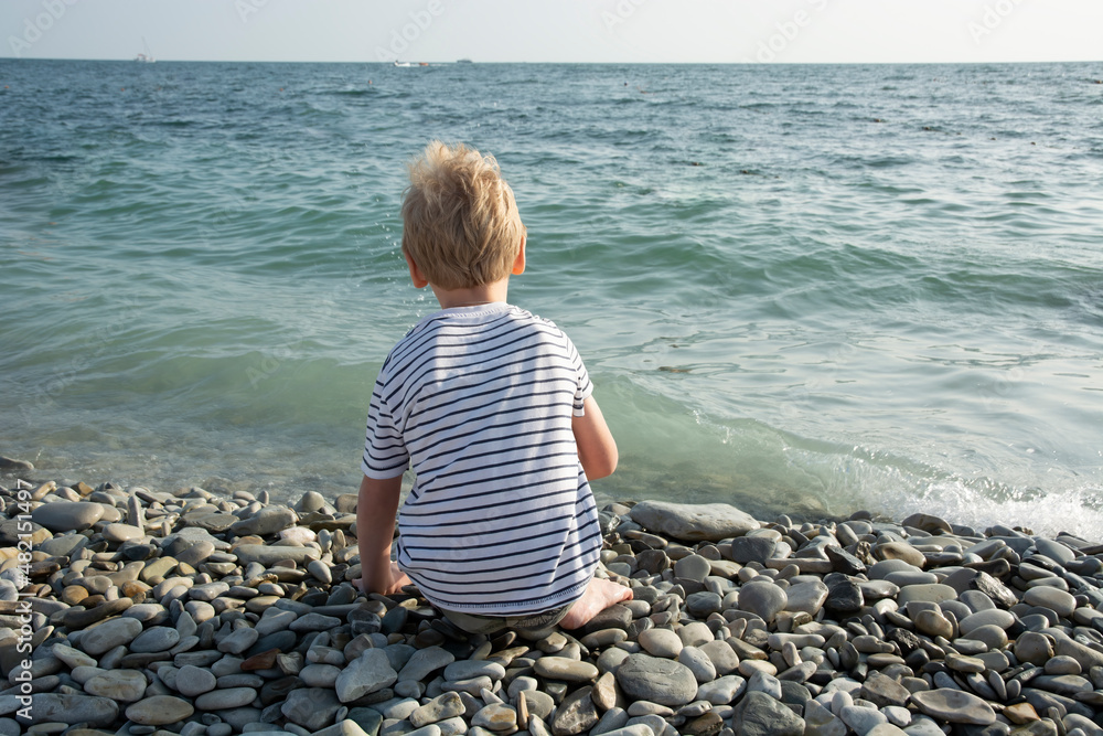 a boy in a striped white T-shirt on the background of the sea from the back