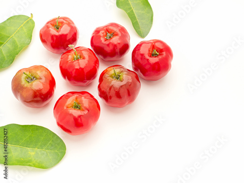 Pile of ripe red acerola cherries and green leaves isolated on a white background.
