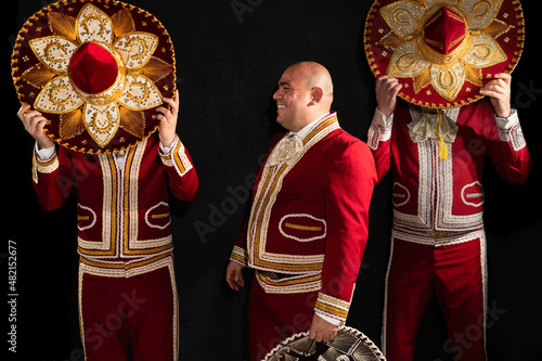 Mexican mariachi musicians cover their faces with a sombrero on a black background. One musician laughs
