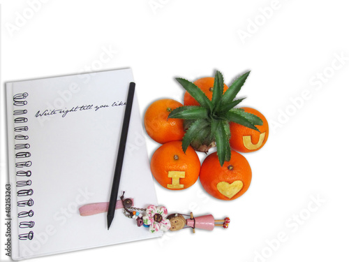 Pencil and wooden doll on notebook with orange in the form of tree and oranges carved symbol “I Love You” on white background.