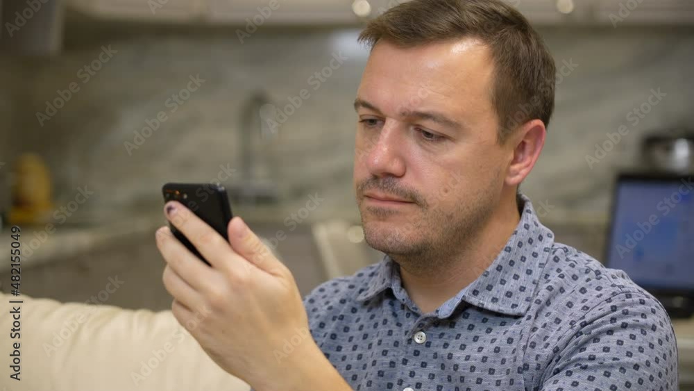 Annoyed millennial man with disgust look at smartphone screen at modern living room. Portrait of manager cringe and looking at phone screen with squeamishness, bad joke or inappropriate content Annoyed millennial man with disgust look at smartphone screen at modern living room. Portrait of manager cringe and looking at phone screen with squeamishness, bad joke or inappropriate content