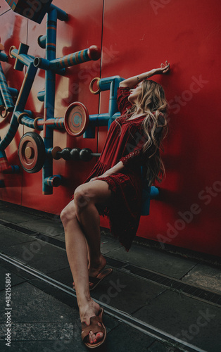 A slender girl with blond long hair in a red dress. Sunny weather girl walks around the city.
