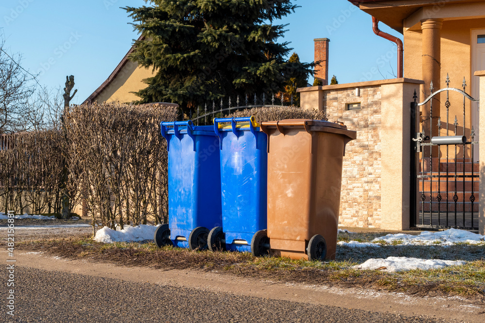 Three plastic recycling bins for the waste sorting in front of a small house in a village Three plastic recycling bins for the waste sorting in front of a small house in a village