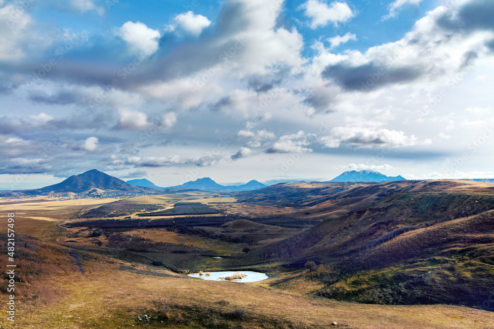 Laccoliths of the North Caucasus. Mountains of Caucasian mineral waters. Beautiful spring landscape with mountain peaks of magmatic origin, blue sky, clouds and sun.