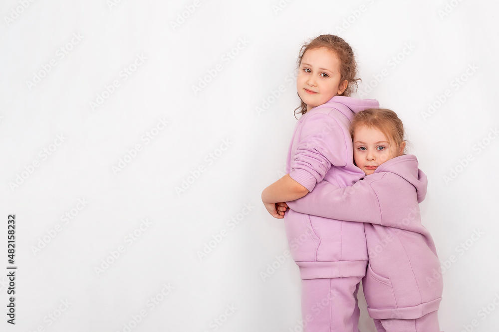Two cute little girls sisters in fashionable spring clothes with a hood.  Carefree children in identical hoodies pose on a white background.