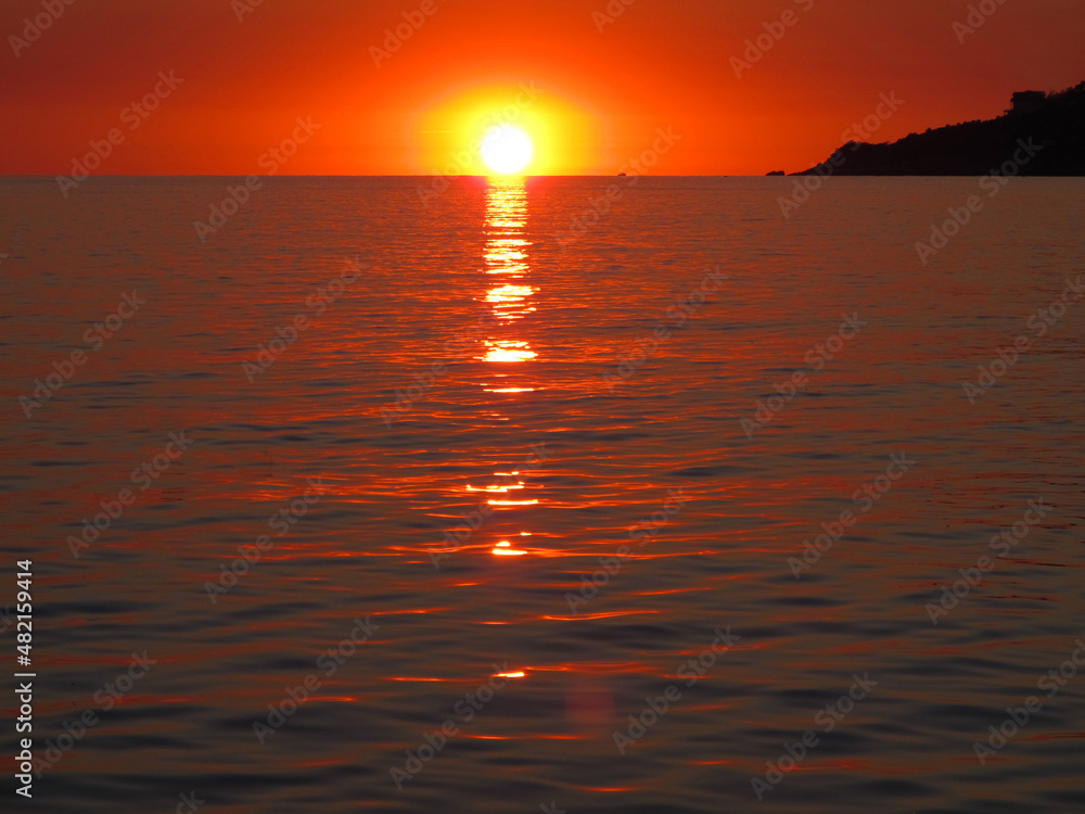 Obraz premium Bright sunset over the sea. The sun on the horizon is reflected on the surface of the water