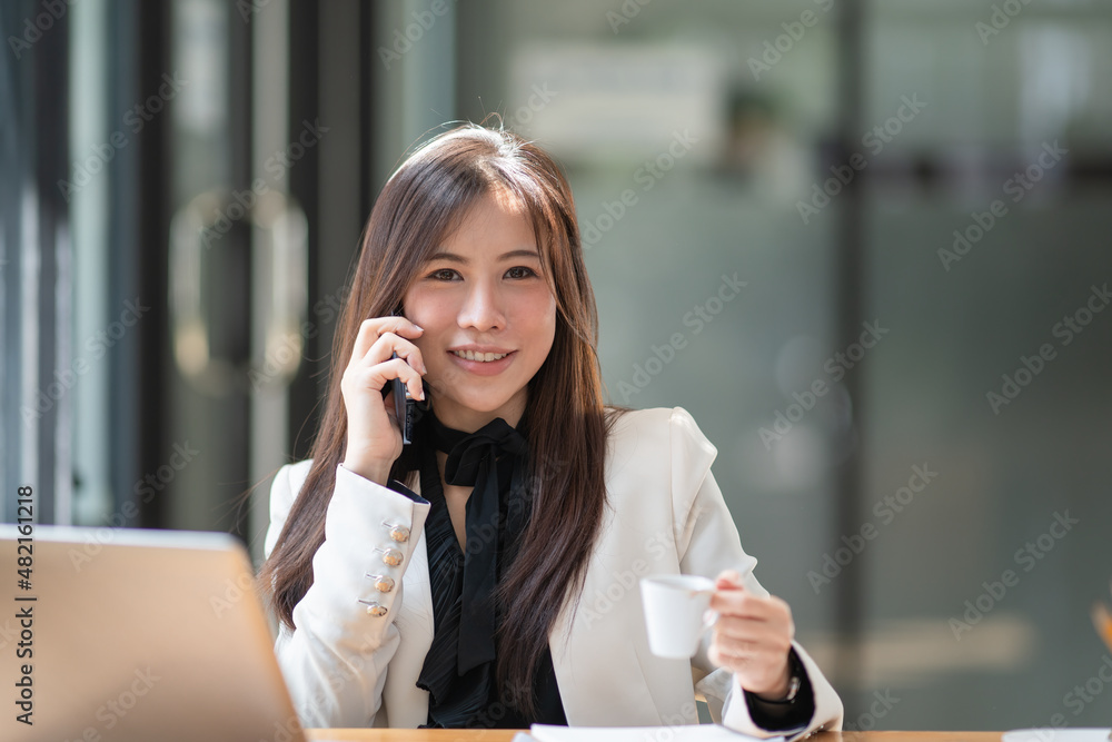 A beautiful Asian woman holding and using a mobile phone while drinking coffee in a cafe. A beautiful Asian woman holding and using a mobile phone while drinking coffee in a cafe.