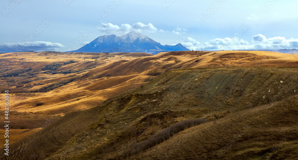 Laccoliths of the North Caucasus. Mountains of Caucasian mineral waters. Beautiful spring landscape with mountain peaks of magmatic origin, blue sky, clouds and sun. Beshtau Mountain.