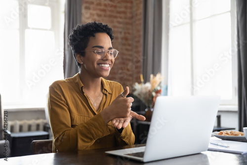 Smiling friendly African American therapist in glasses talking on video call, using sign language, speaking to patient with hearing disability, deafness, showing gestures at screen photo