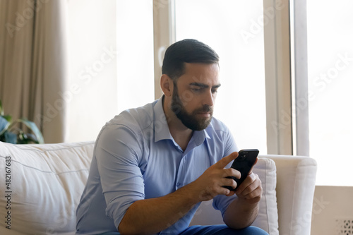 Focused millennial mobile phone user man chatting online, reading text message, surfing social media, Internet, using online app for communication. Businessman checking messenger, email on smartphone