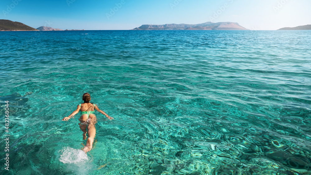 Panoramic view of summer girl in green swimsuit bikini swimming in clear turquoise sea water. Vacation at Paradise. Ocean relax, travel to island