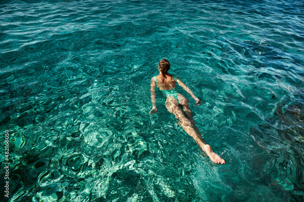 Top view swimming woman in green swimsuit bikini enjoying in blue sea water, tropical beach destination, inspiration travel vacation