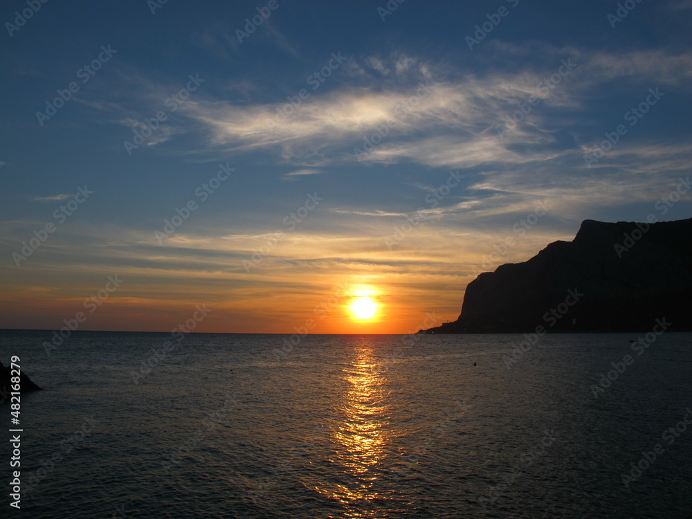 Beautiful sunset on the sea, mountain silhouette and orange sun on the horizon, Crimea, Black Sea