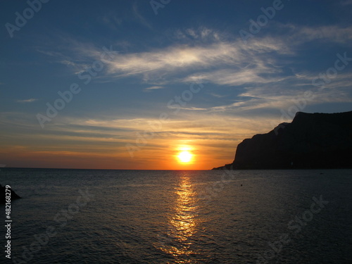 Beautiful sunset on the sea, mountain silhouette and orange sun on the horizon, Crimea, Black Sea © Vasilisa