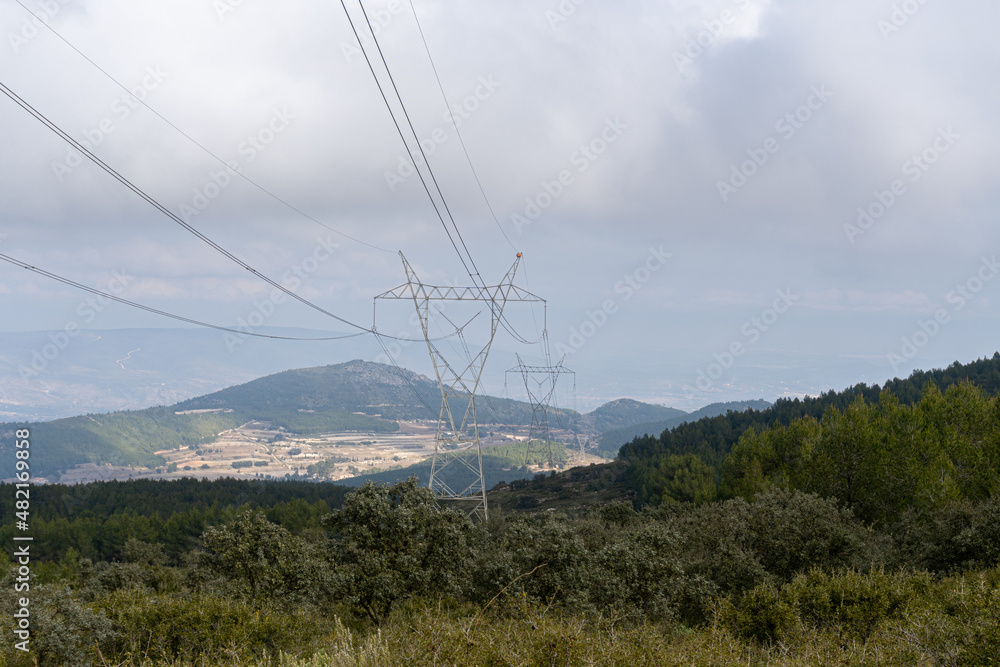 High voltage power lines over a Mediterranean forest on a cloudy and rainy day.