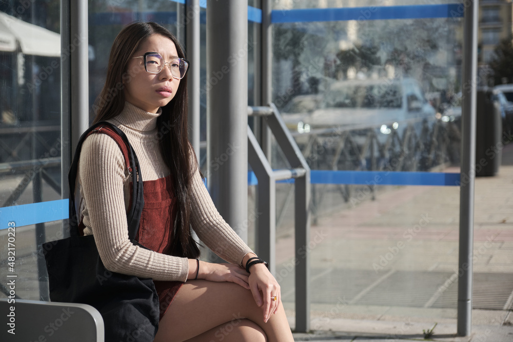 Young asian woman waiting for the bus at bus stop.