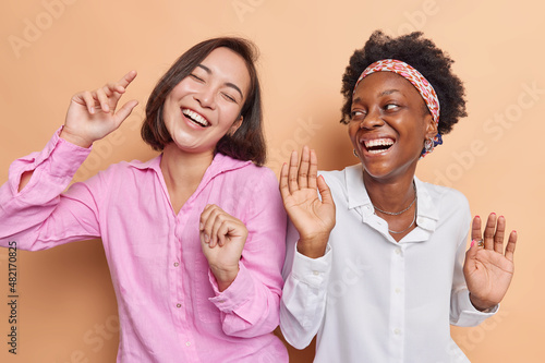 Magnificent diverse female friends dance carefree move with rthythm of music spend time together on party have good mood isolated over beige background. People friendship fun emotions concept photo