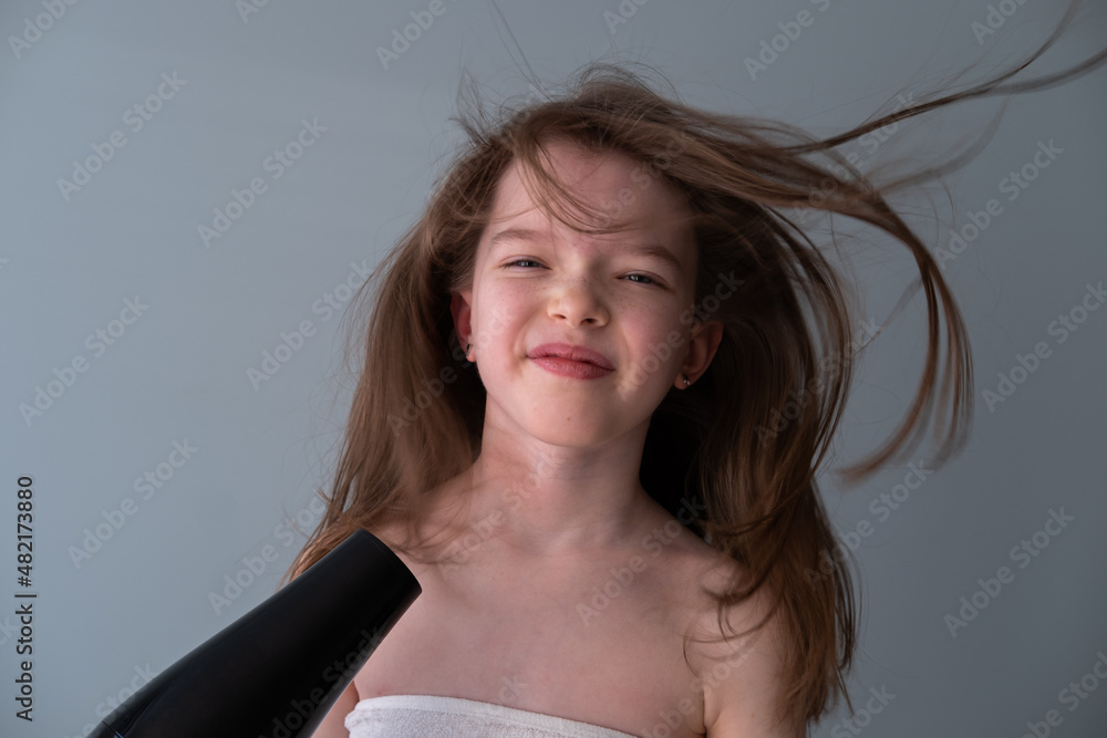 Little girl dries her hair with a hairdryer, portrait