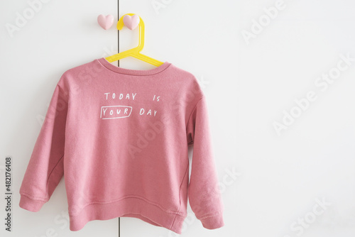 one children's pink sweater hangs on a yellow hanger on a white wardrobe with heart handles with the inscription today is your day, place for text