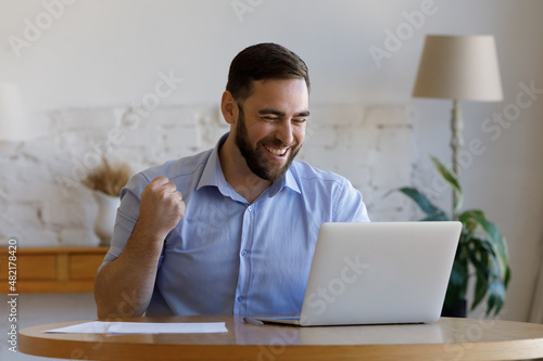 Fotografia Excited happy millennial guy getting good news, looking at laptop display, smiling, reading email message, bank notice, laughing, making sinner gesture