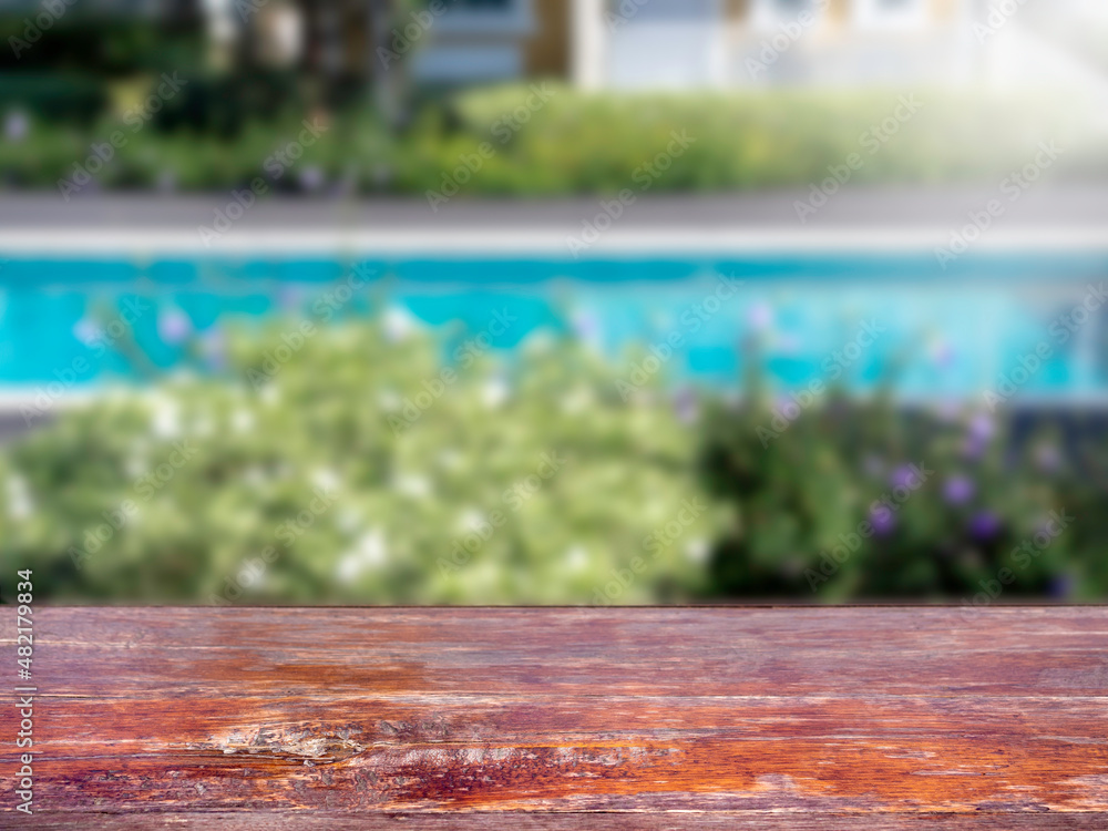 Close up empty grunge wooden top table in front of a swimming pool on sunny day, poolside view, blurred background.