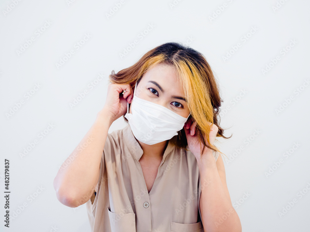 Happy smiling woman in sleeveless shirt with short brown hair and highlights wearing a white protective face mask by two hands on white background. Female portrait with a medical face mask. Happy smiling woman in sleeveless shirt with short brown hair and highlights wearing a white protective face mask by two hands on white background. Female portrait with a medical face mask.
