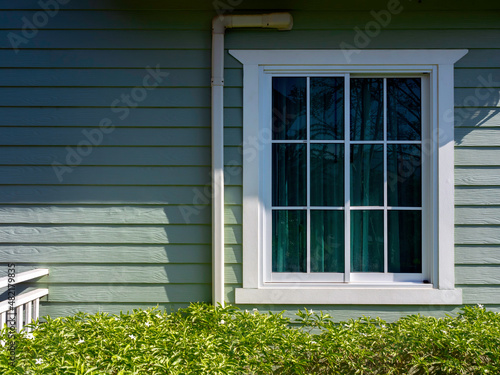 A white house window with glass, green curtain decoration on the small light green wooden resident with copy space, view from outdoor.