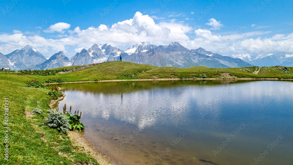 A man jumping at the Koruldi Lake with an amazing view on mountain ridges near Mestia in the Greater Caucasus Mountain Range, Upper Svaneti, Country of Georgia. Reflection in the water. Wanderlust.