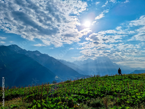 A man enjoying the amazing view on the valley of Mestia in the Greater Caucasus Mountain Range,Country of Georgia.The sun rays are hitting the alpine pasture,generating a magical atmosphere.Wanderlust